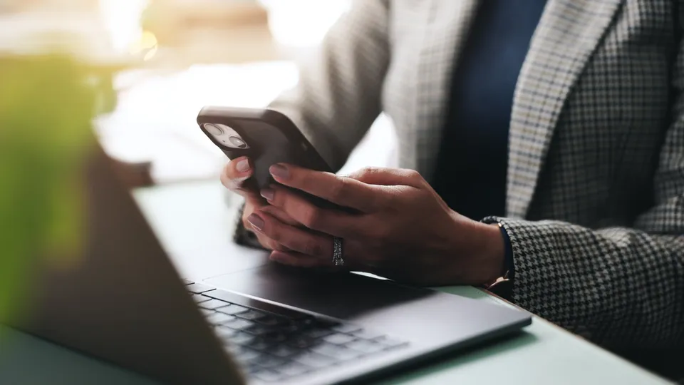 Iemand gebruikt een telefoon aan een laptop