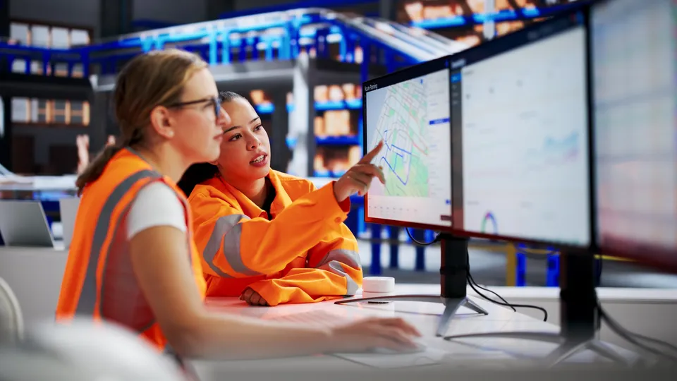 Two operators in high-visibility jackets at control room screens
