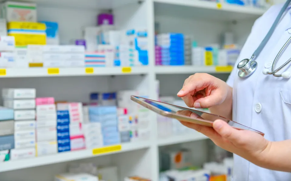 A pharmacist with a tablet at pharmacy shelves