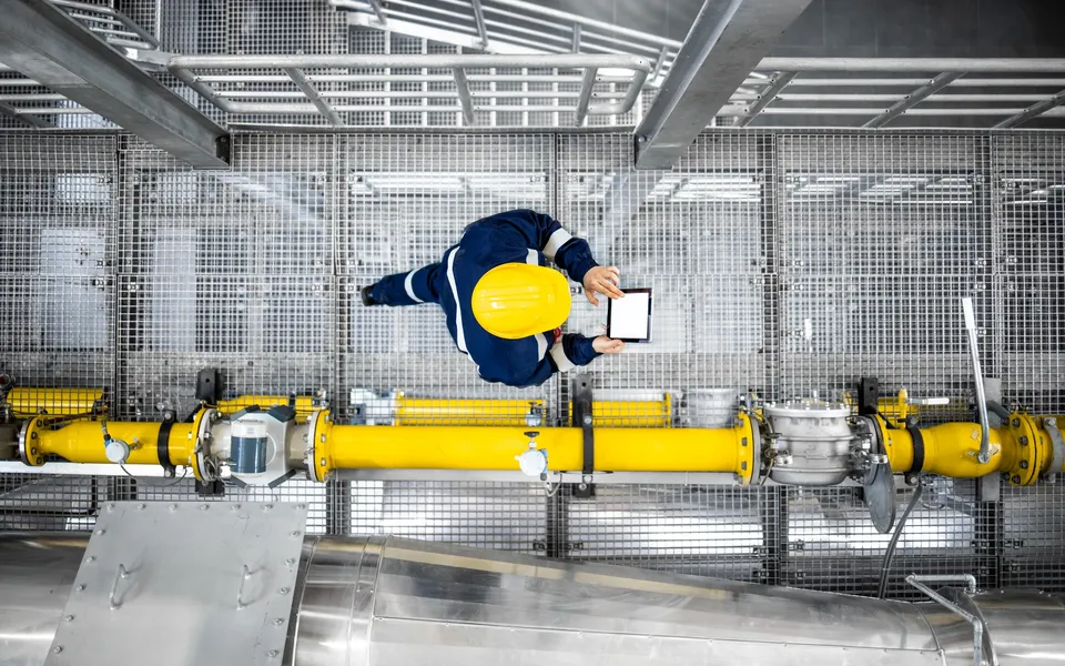 An industrial plant interior with a worker among the pipes, seen from above